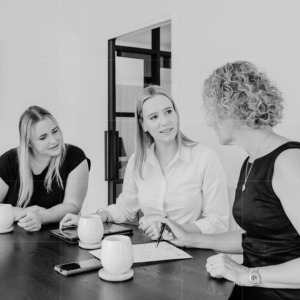 Three team members in a business meeting reviewing paperwork, discussing compliance strategies and client support planning.