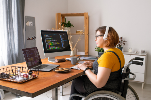 Young woman in wheelchair working from her home office and eating morning tea
