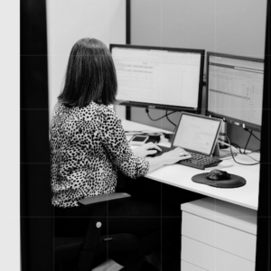 Professional woman working at a desk with multiple computer monitors, focused on data and reports.