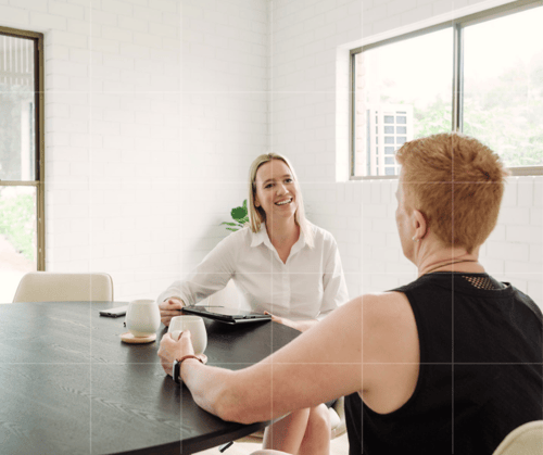 Two people at a table in a modern office. One with short blond hair is an accountant, the other is her client and has short red hair.