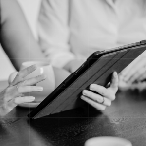 Two professionals discussing information on a tablet over coffee in a business setting.