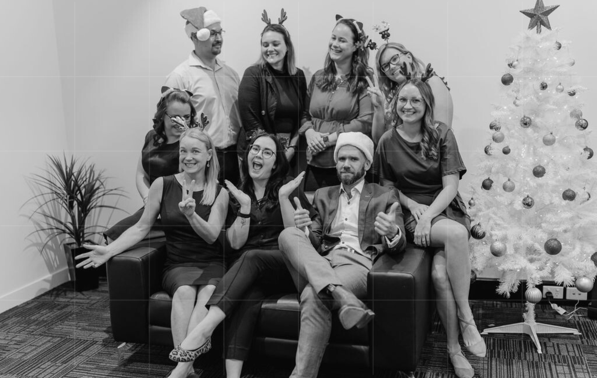 Business team celebrating the holiday season with Santa hats and reindeer antlers by a Christmas tree, capturing festive camaraderie and the focus on managing cash flow during Christmas.