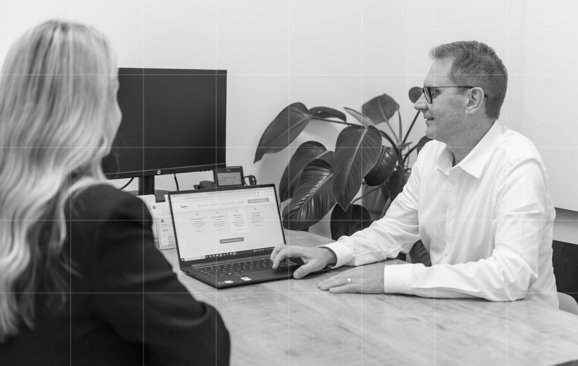 Business consultation between two professionals in an office, with a laptop displaying a financial website.