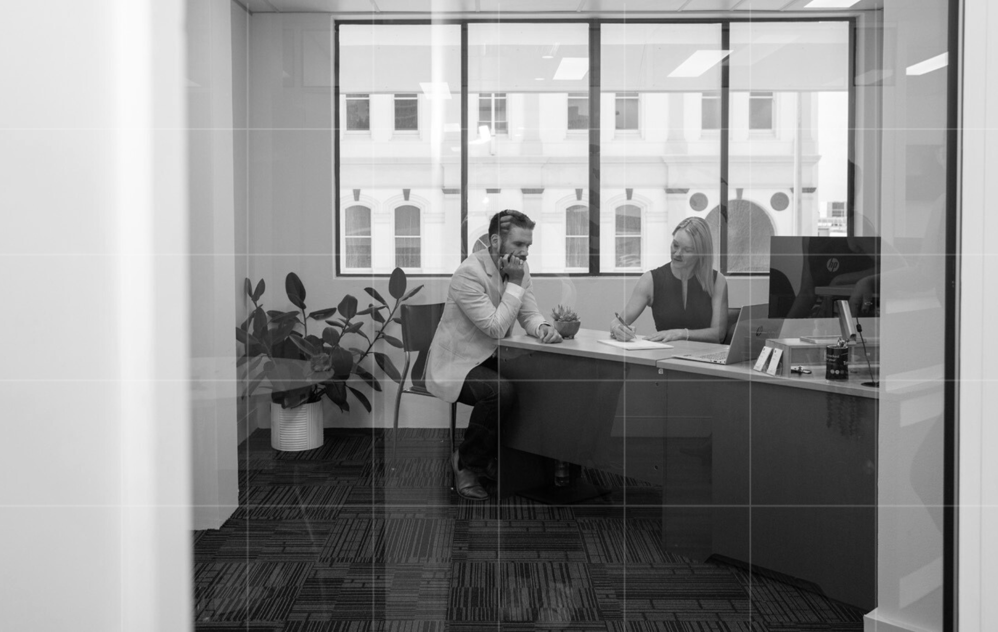 Professional business consultation in a modern office, featuring a client and advisor in discussion with notes and a laptop on the desk.