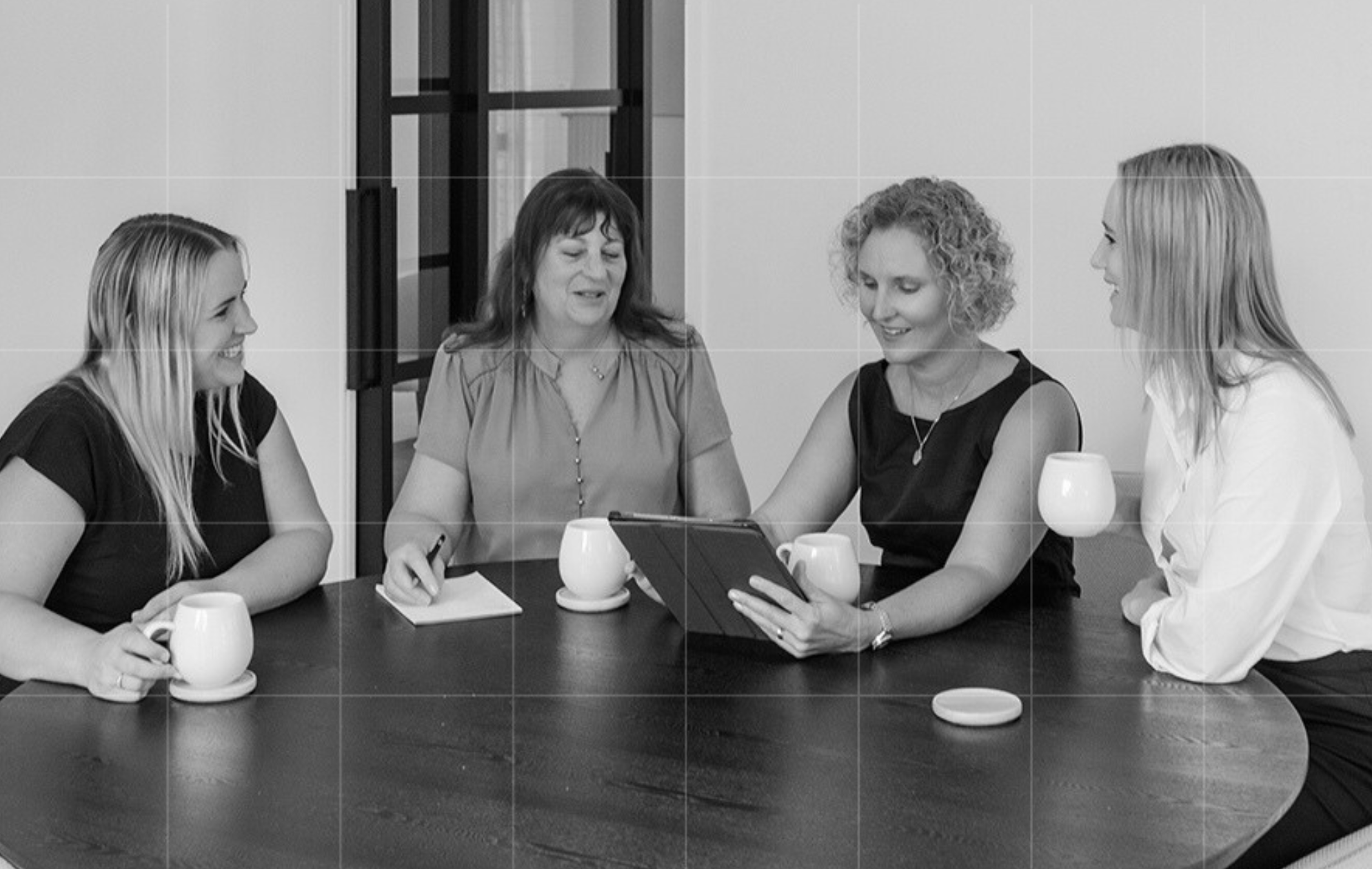 Group of Trekk Advisory advisors gathered around a table with coffee cups, reviewing bookkeeping notes on a tablet in a collaborative discussion.