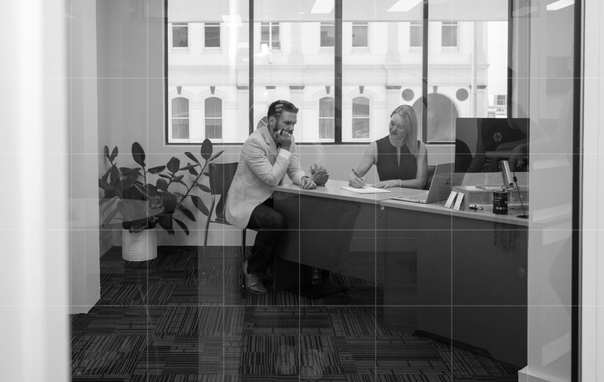 Two colleagues at Trekk Advisory - North Queensland office chatting at a desk in a bright, plant-filled office with glass walls.