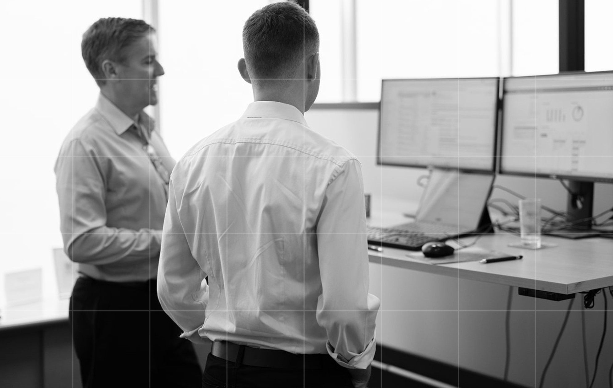 Trekk Advisory team members standing at a desk reviewing data on dual computer monitors, business advisory discussion
